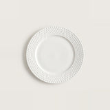 A white ceramic plate with a textured, dimpled pattern around the rim, centered on a light beige background.