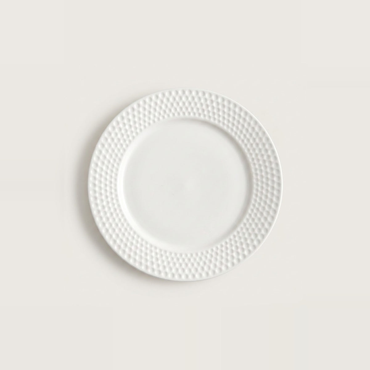 A white ceramic plate with a textured, dimpled pattern around the rim, centered on a light beige background.