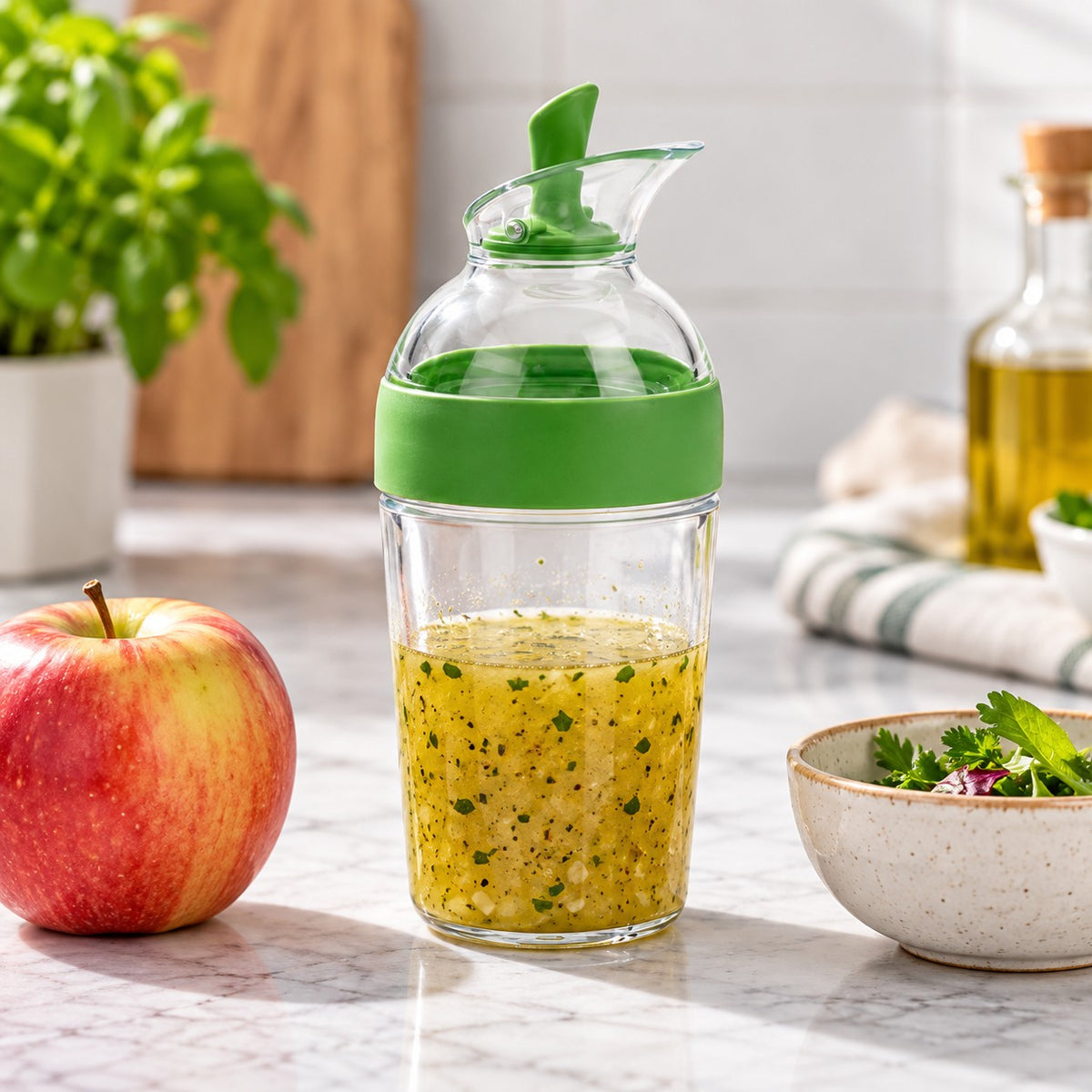 Green 240 ml Salad Dressing Shaker stands beside an apple and small bowl on a kitchen counter.