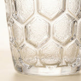 Close-up of a clear textured glass tumbler with a honeycomb pattern, showing the embossed details and transparent material.