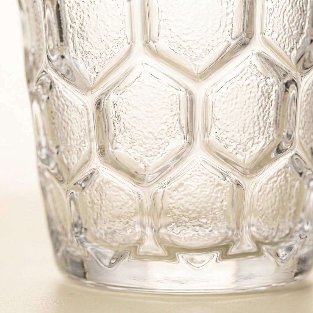 Close-up of a clear textured glass tumbler with a honeycomb pattern, showing the embossed details and transparent material.