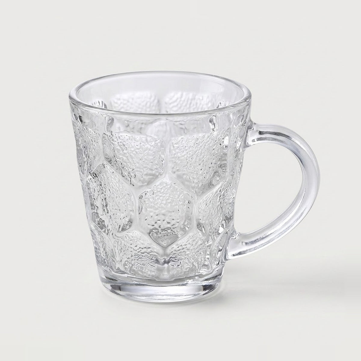 A clear textured glass mug with a honeycomb pattern and a curved handle, shown on a light gray background.