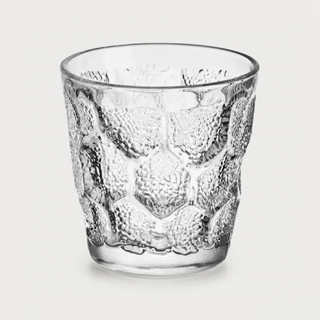A clear textured glass tumbler with a raised honeycomb pattern, shown on a light gray background.