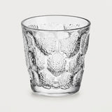 A clear textured glass tumbler with a raised honeycomb pattern, shown on a light gray background.