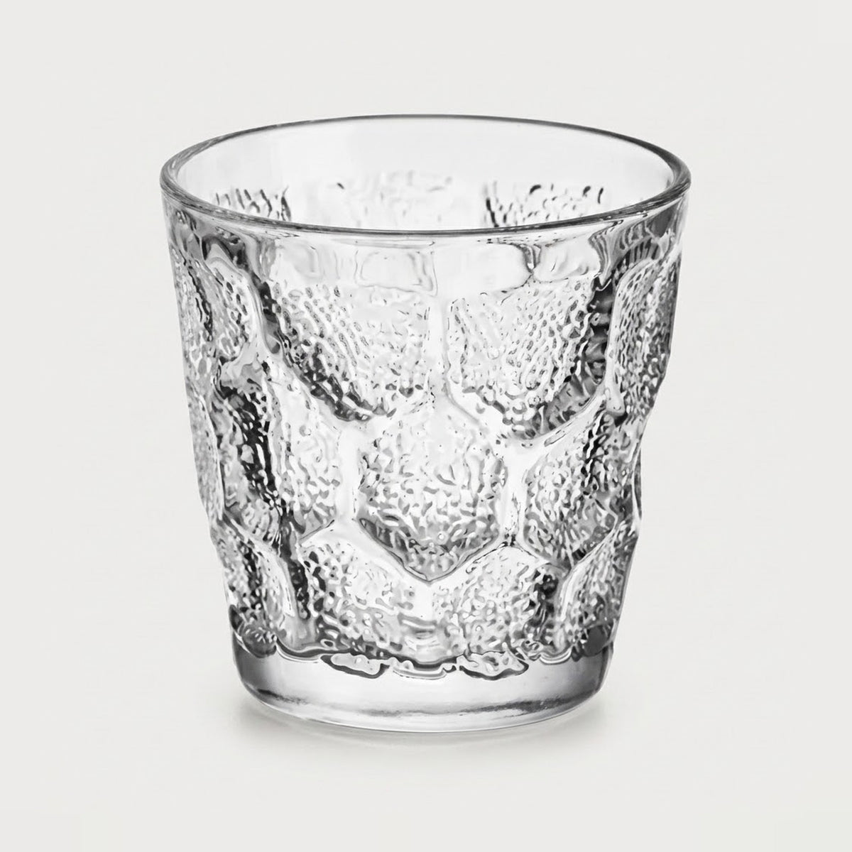 A clear textured glass tumbler with a raised honeycomb pattern, shown on a light gray background.