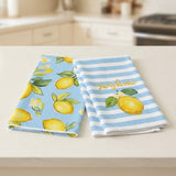 Two folded kitchen towels on a light countertop. One towel has a light blue background with yellow lemons and green leaves.