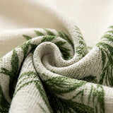 A close-up of a knitted textile with a green leaf pattern on an off-white background, arranged in a spiral to show the fabric texture.
