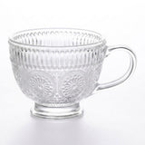 A clear glass teacup with embossed floral and vertical ribbed patterns, set against a plain white background.