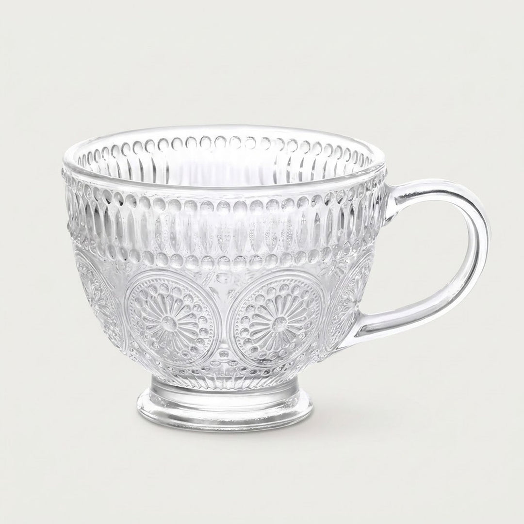 A clear glass teacup with embossed floral and vertical ribbed patterns, set against a solid light gray background.