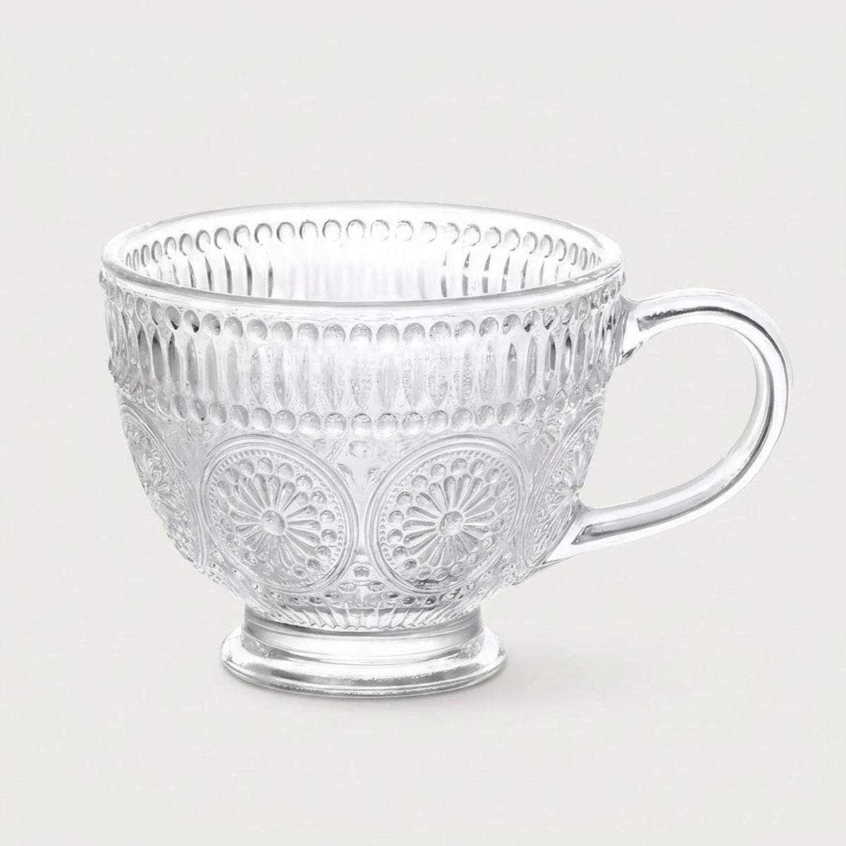 A clear glass teacup with embossed floral and vertical ribbed patterns, set against a solid light gray background.