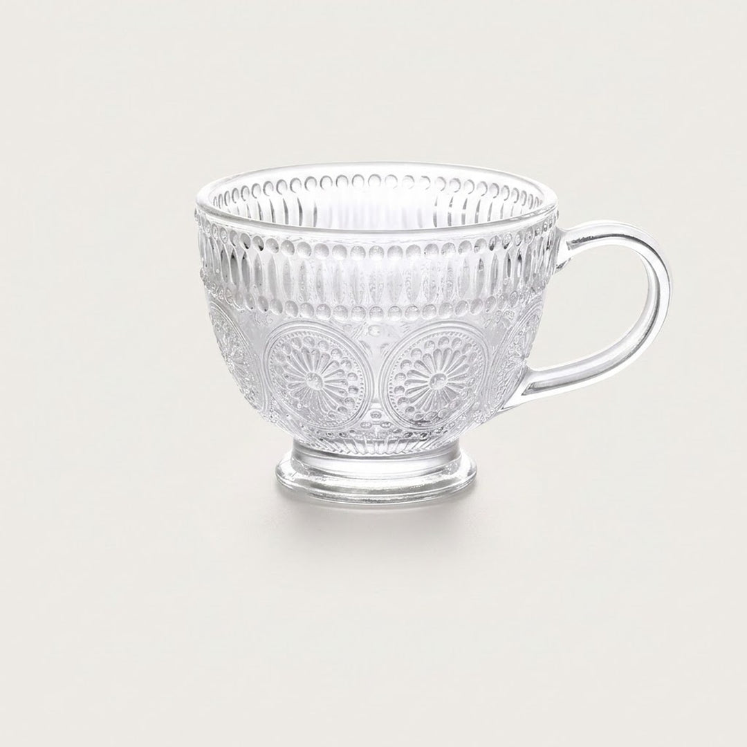A clear glass teacup with embossed floral and vertical ribbed patterns, set against a solid light beige background.