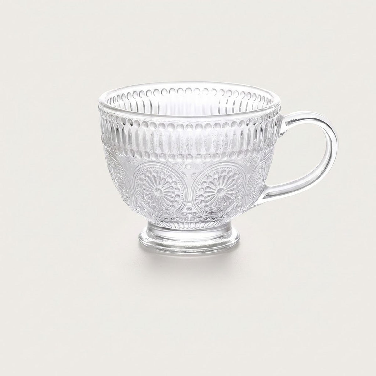A clear glass teacup with embossed floral and vertical ribbed patterns, set against a solid light beige background.
