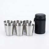 Six small stainless steel shot glasses arranged in two rows next to a black textured cylindrical carrying case on a white background.