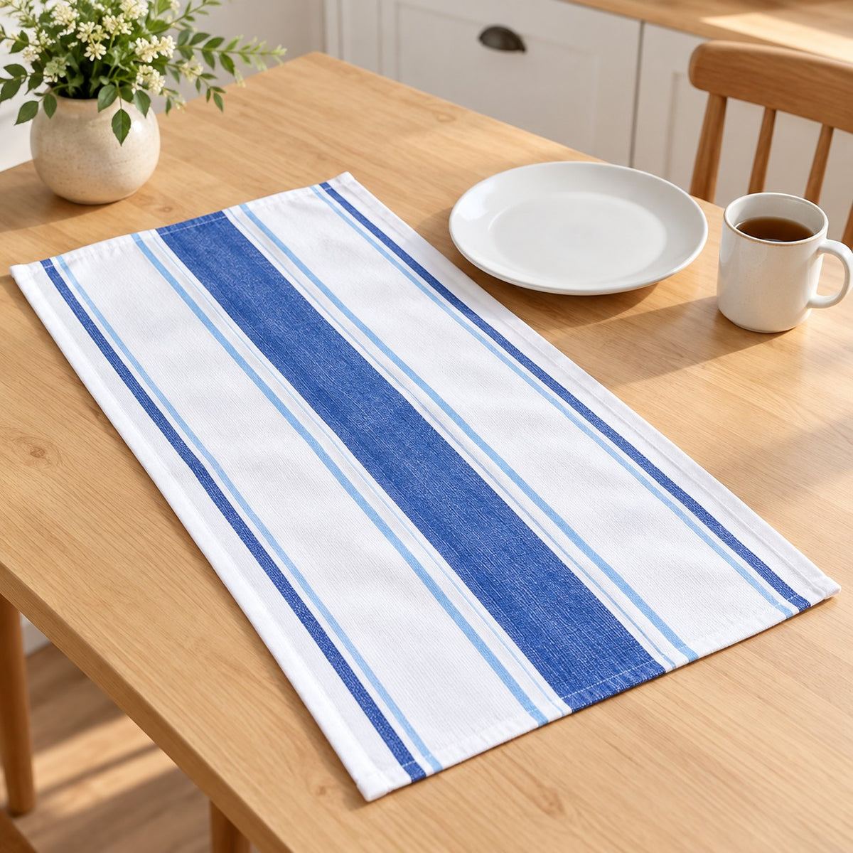Blue striped cotton tea towel is laid beside a dinner plate and mug to show its table scale.