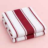 Red striped cotton tea towel folded on a pale blush studio background.