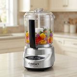 Cuisinart Mini Prep Plus food chopper with a silver base, clear container, and black handle, shown blending colorful vegetables on a kitchen countertop.