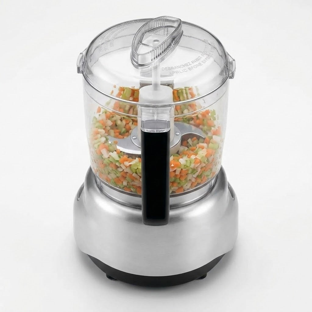 A countertop food processor with a clear plastic bowl filled with chopped vegetables, a silver metal base, and a black handle, shown on a clean white background.