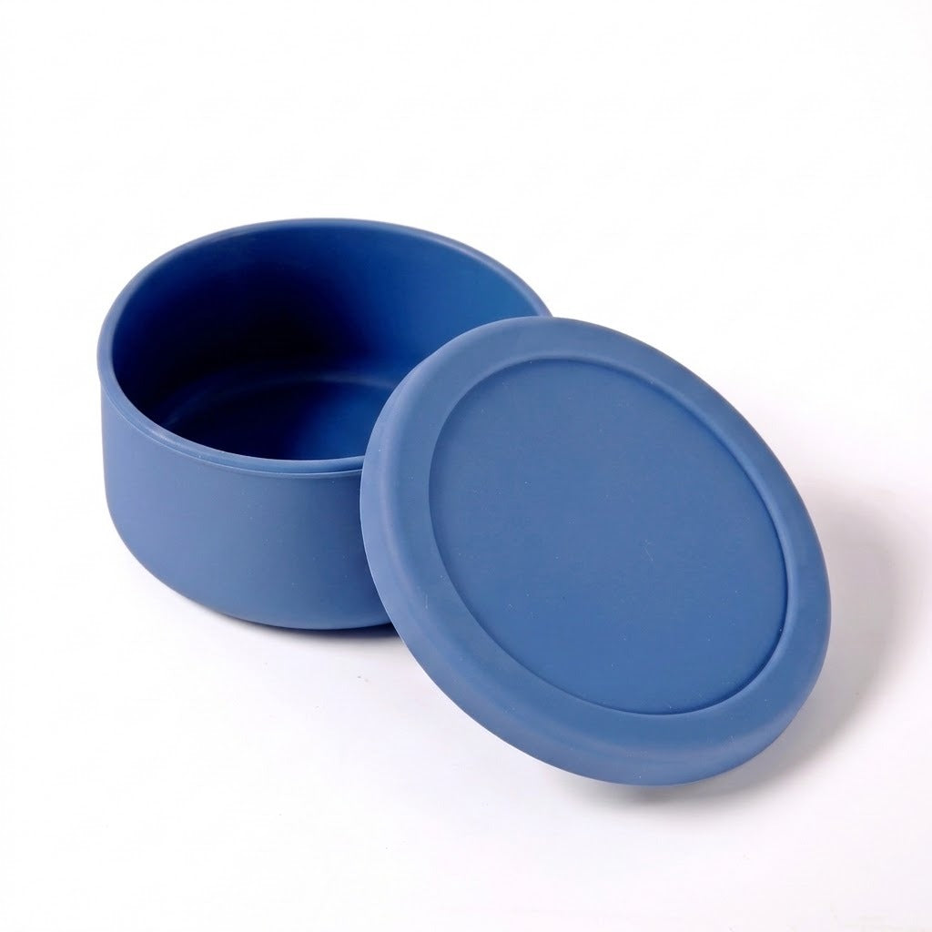 A blue silicone container with its matching lid leaning against it, shown on a clean white background.