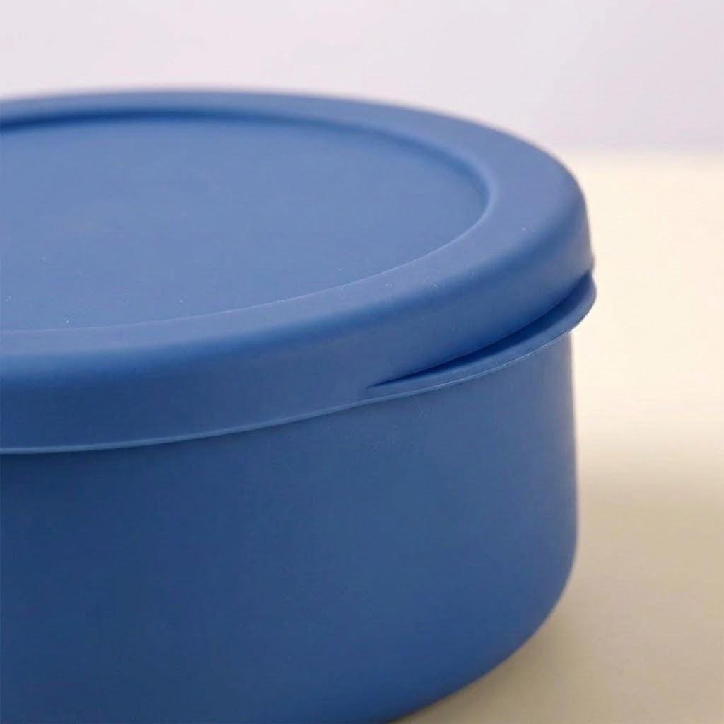 A close-up of a blue round plastic container with a matching lid, shown on a light neutral background.