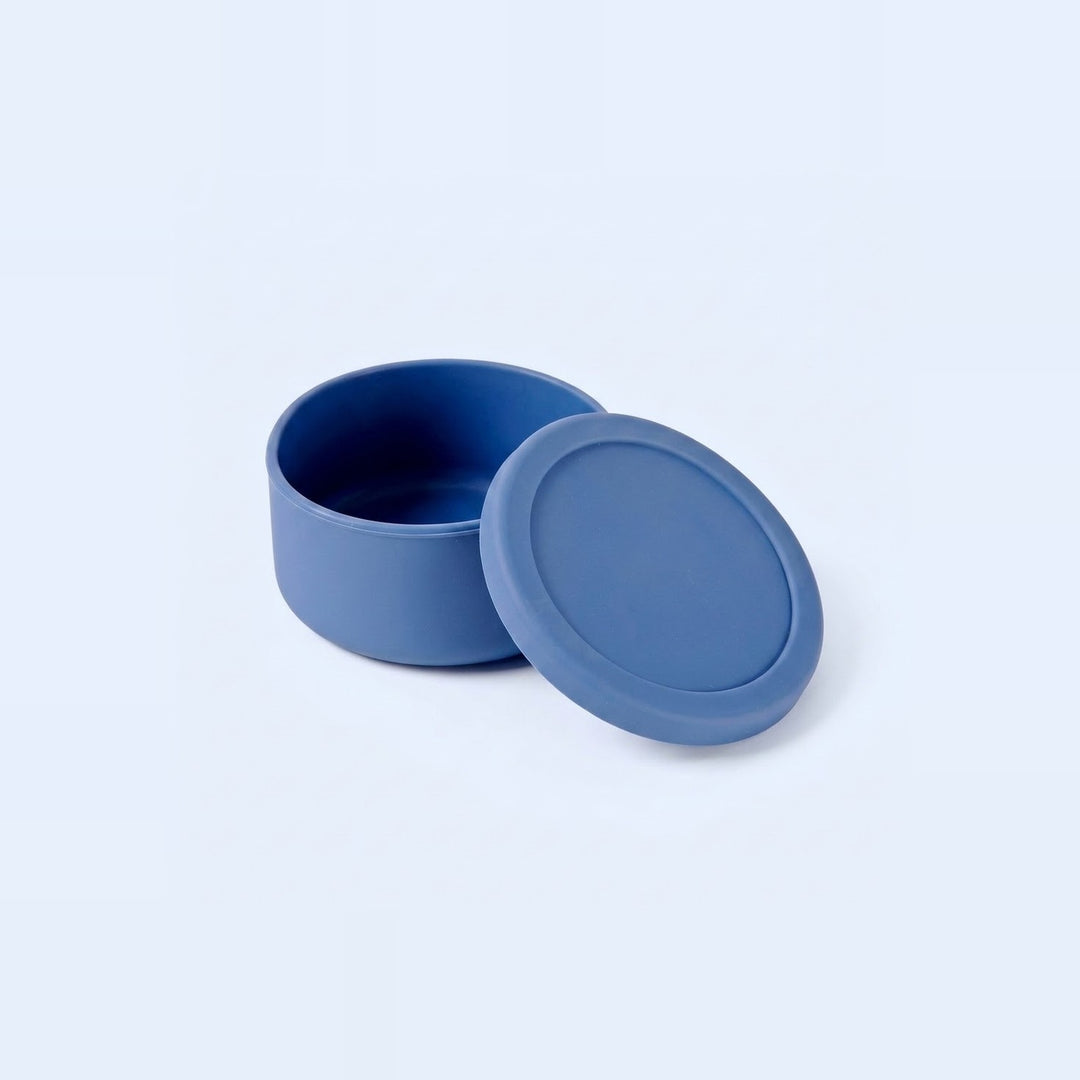 A small round blue container with its lid leaning against it, photographed on a clean light gray studio background.