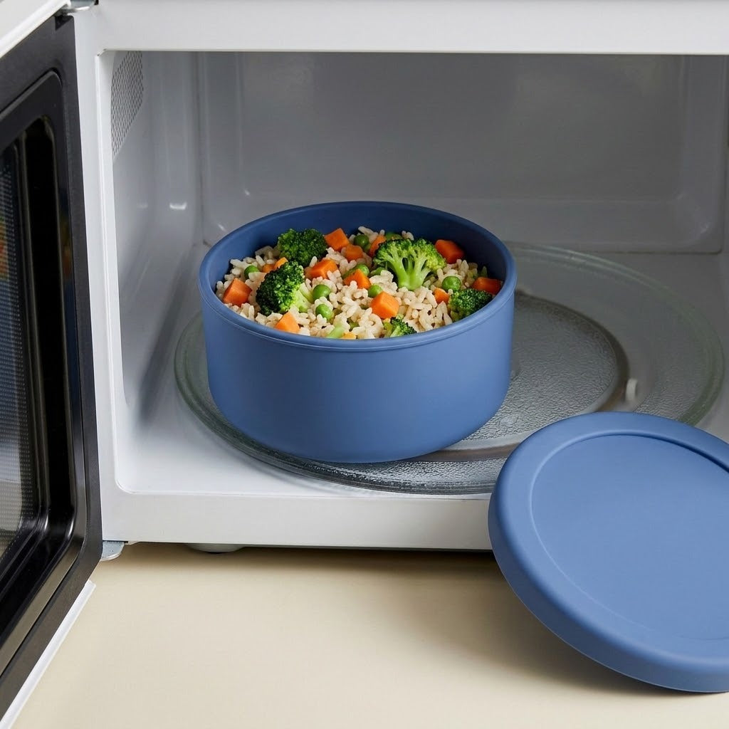 A blue silicone microwave insert bowl filled with cooked rice and mixed vegetables, sitting inside a white microwave, with the matching blue lid resting on the counter beside it.
