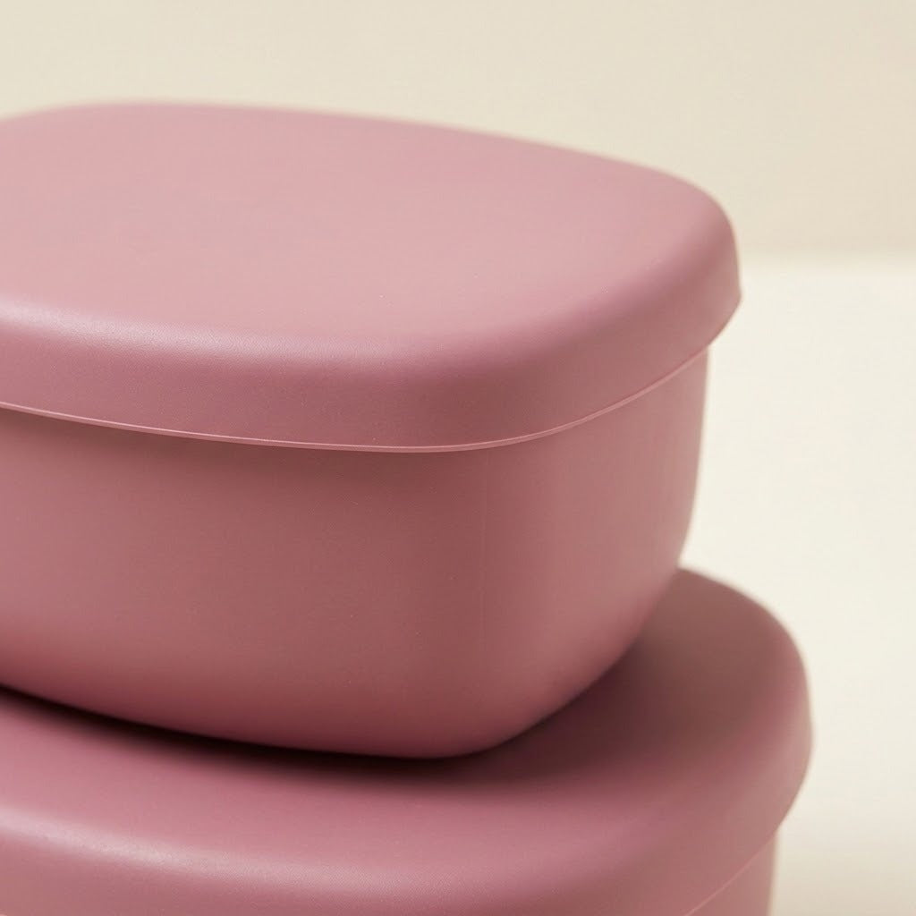 A close-up of a dusty pink plastic container with a matching lid, stacked on top of another container against a light cream background.
