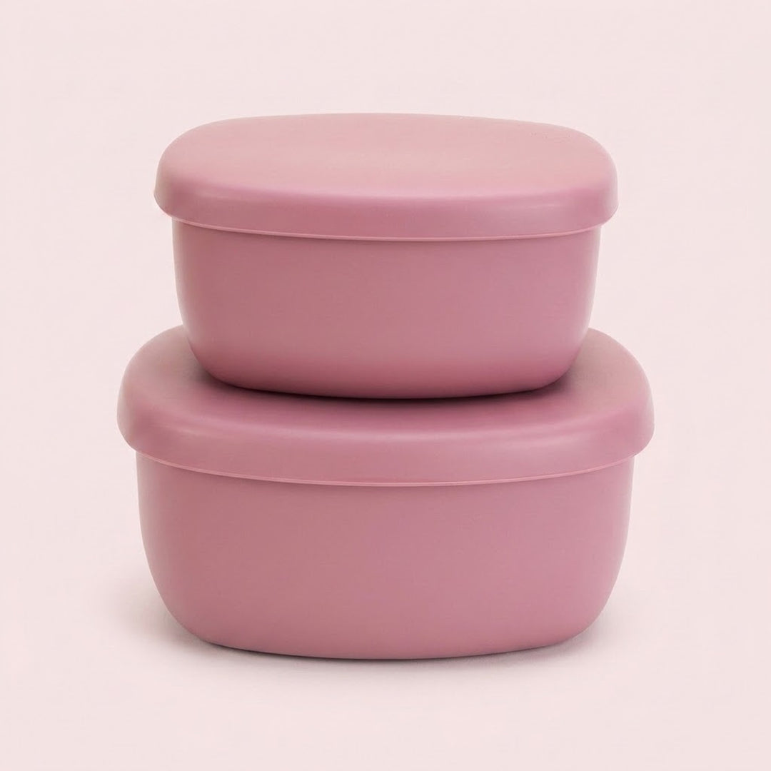 Two stacked dusty pink silicone food storage containers with matching lids, set against a solid pale pink background.