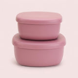 Two stacked dusty pink silicone food storage containers with matching lids, set against a solid pale pink background.