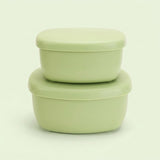 Two stacked light green plastic food storage containers with matching lids, photographed on a clean, solid, very pale green background.