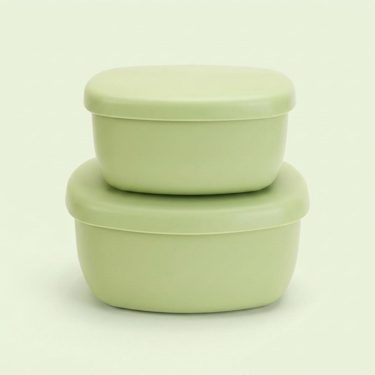 Two stacked light green plastic food storage containers with matching lids, photographed on a clean, solid, very pale green background.