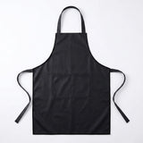 A black bib apron with a neck strap, waist ties, and a front pocket, laid flat against a white background.