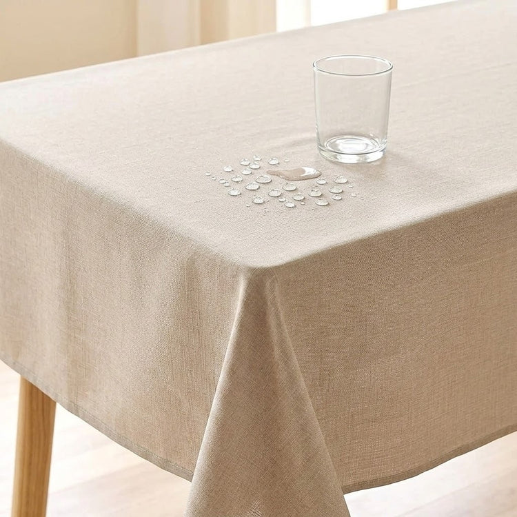 A beige tablecloth draped over a table, with a clear glass tumbler and a small water droplet spill on top to demonstrate water resistance.