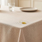 A beige linen tablecloth draped over a table, with a small decorative gold and silver centerpiece and a glass of water in the softly blurred background.