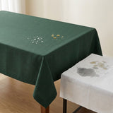 A dark green tablecloth draped over a rectangular table in a bright room, with a second white tablecloth showing water spots in the foreground.