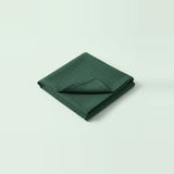A folded dark green fabric item, likely a napkin or small cloth accessory, photographed on a clean light gray studio background.