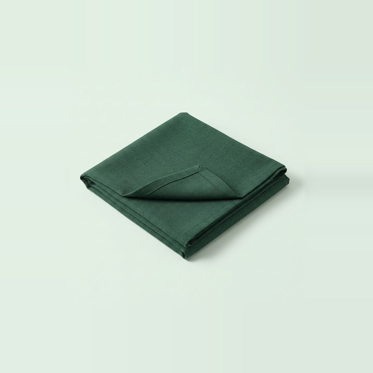 A folded dark green fabric item, likely a napkin or small cloth accessory, photographed on a clean light gray studio background.
