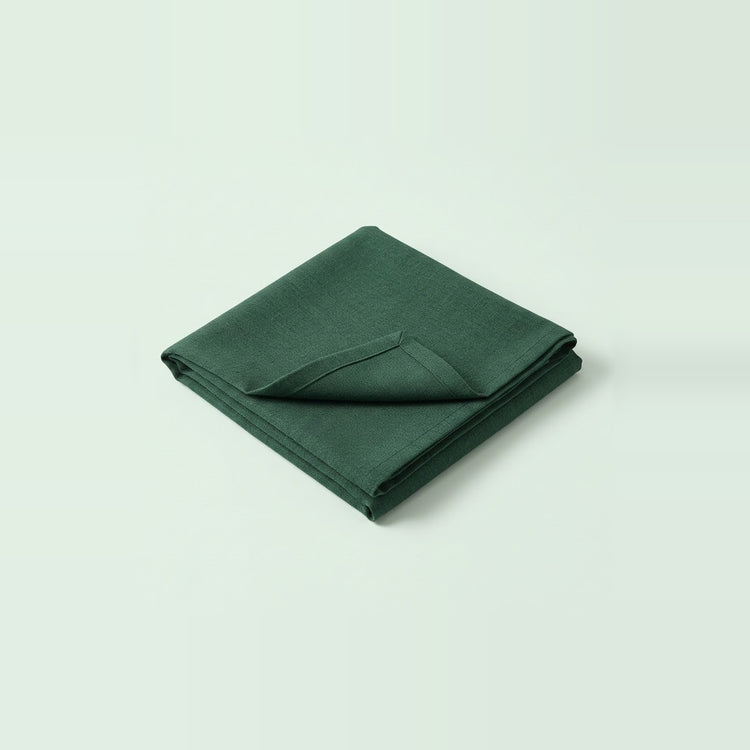 A folded dark green fabric item, likely a napkin or small cloth accessory, photographed on a clean light gray studio background.