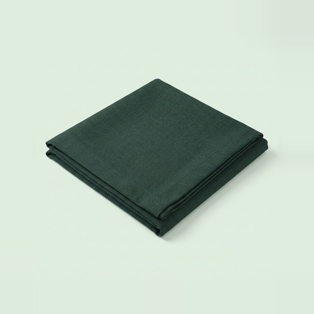 A folded dark forest green fabric item, likely a napkin or cloth, shown on a clean, solid, very light off-white background.