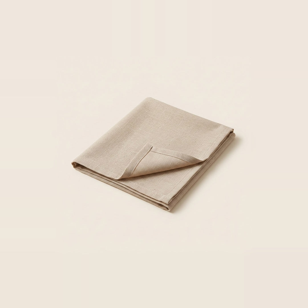 A folded beige linen napkin with a pointed corner, displayed on a solid cream background.