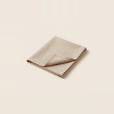 A folded beige linen napkin with a pointed corner, displayed on a solid cream background.