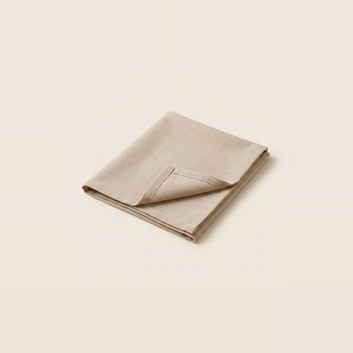 A folded beige linen napkin with a pointed corner, displayed on a solid cream background.