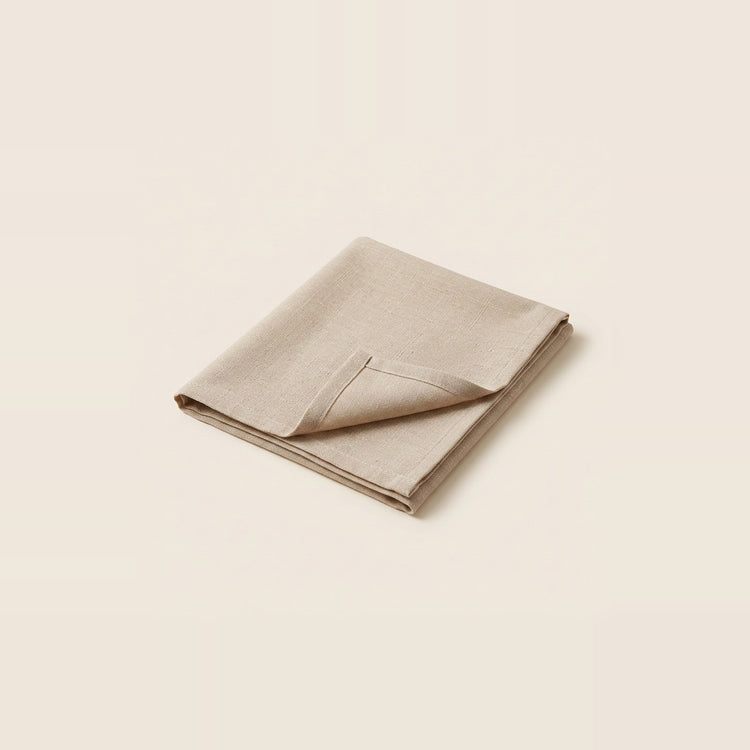 A folded beige linen napkin with a pointed corner, displayed on a solid cream background.