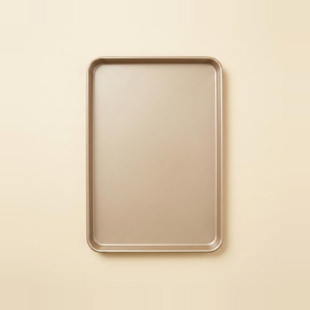 A rectangular metal baking pan with rounded corners, shown from a top-down view on a solid, warm cream-colored background.