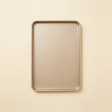 A rectangular metal baking pan with rounded corners, shown from a top-down view on a solid, warm cream-colored background.