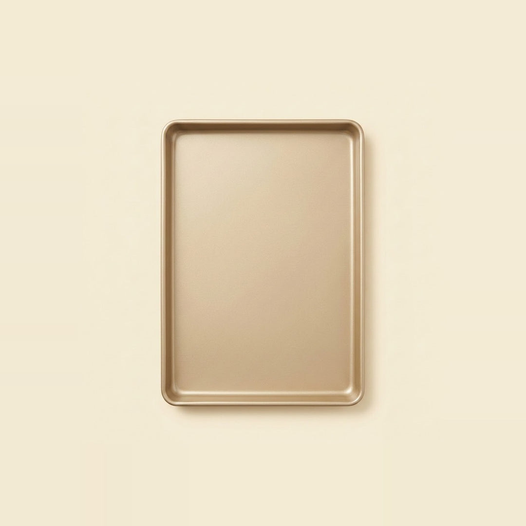 A rectangular metal baking pan with rounded corners, shown from a top-down view on a solid, warm cream-colored background.