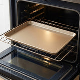 A rectangular metal baking sheet with raised edges, shown resting on a wire rack inside an open oven.