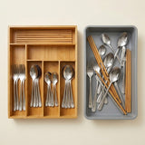 A flat-lay view of a silver-colored dinnerware set with wooden chopsticks, shown in two storage organizers: a light natural bamboo compartment organizer on the left and a gray tray on the right.