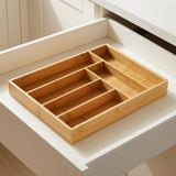 A rectangular bamboo drawer organizer with multiple compartments, shown inside an open white drawer.