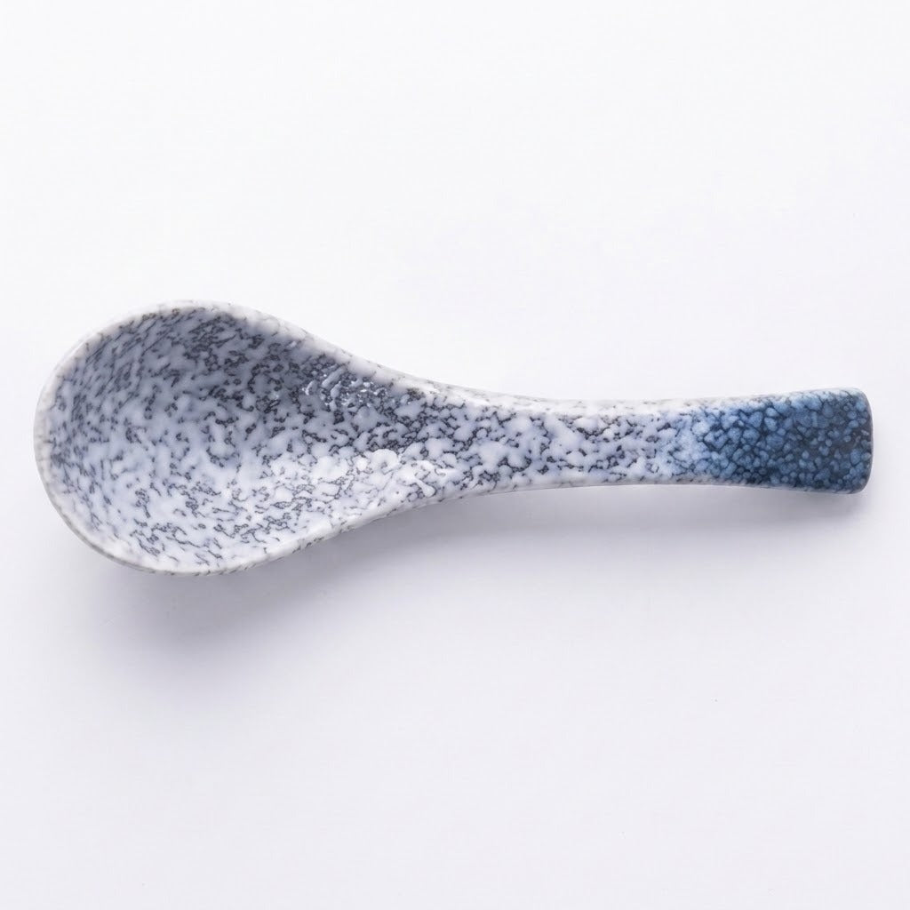A ceramic spoon with a speckled glaze transitioning from white and gray at the bowl to a deep blue at the handle, shown on a plain white background.