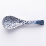A ceramic spoon with a speckled glaze transitioning from white and gray at the bowl to a deep blue at the handle, shown on a plain white background.